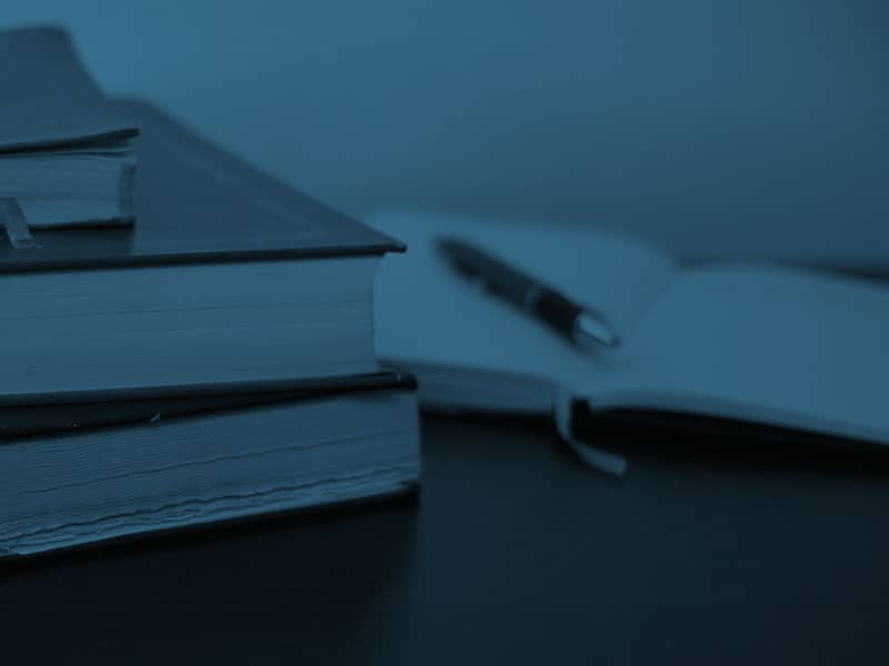 A stack of books and a pen on a table.