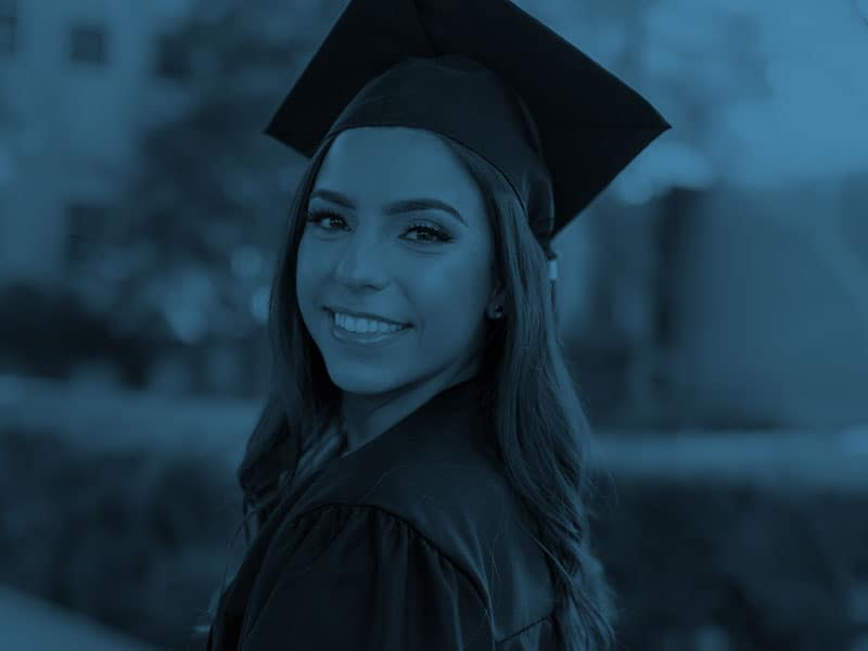 A woman in a graduation gown smiles for the camera.