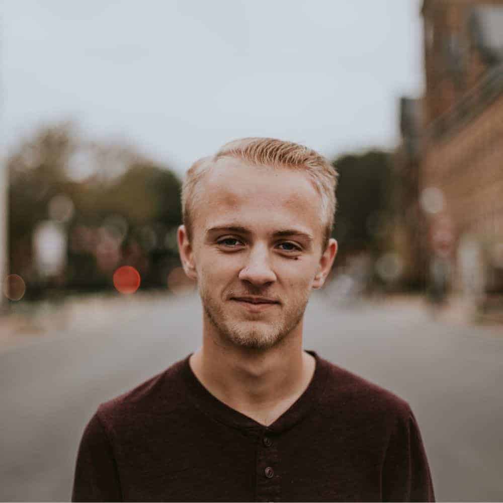 A young man in a maroon shirt standing on a street.