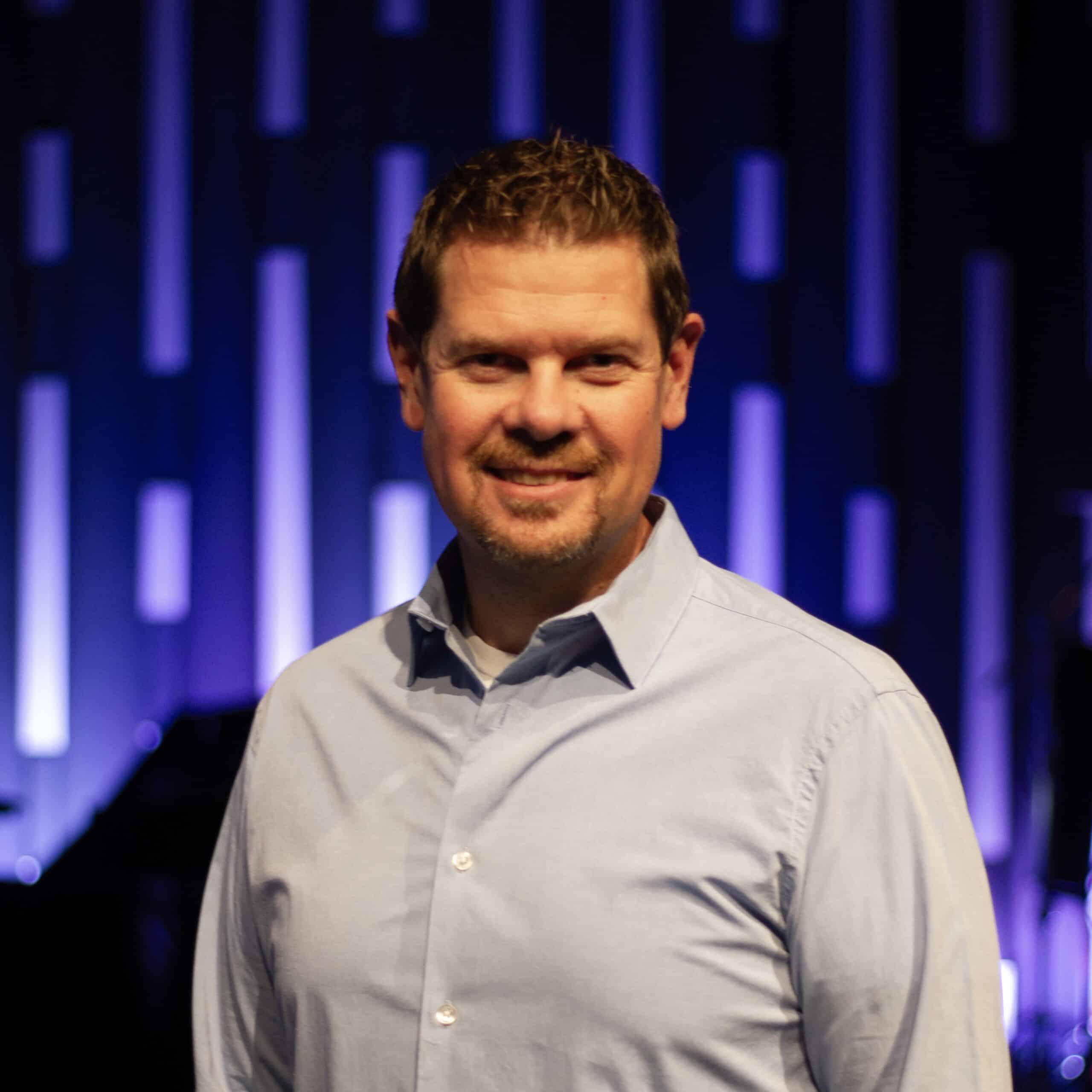 A man in a blue shirt standing in front of a stage.