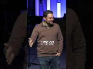 A man stands on stage extending his right hand, with text overlay reading "FIND OUT IF THEY WON." Vertical purple lights are visible in the background.