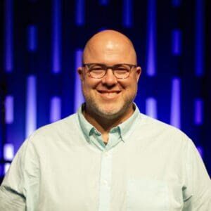 A bald man smiling in front of a blue background.